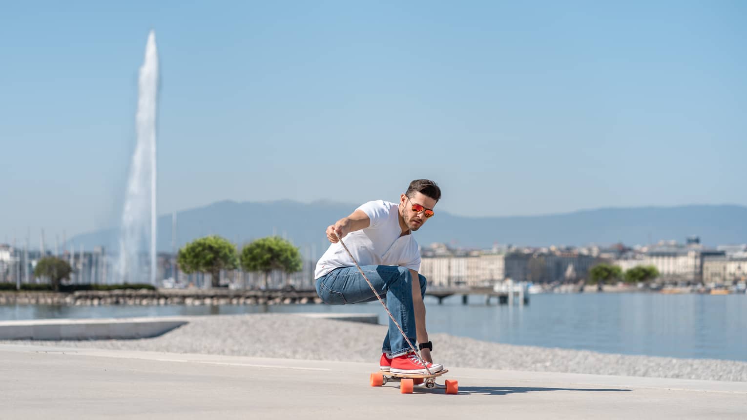 Man longboarding on sidewalk along Lake Geneva with Jet d'Eau fountain in backdrop