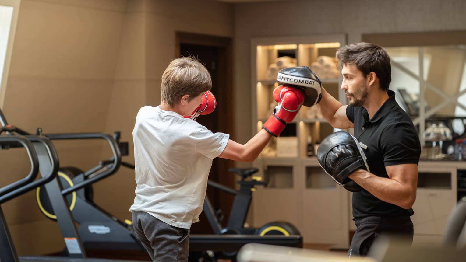 Teenager in red boxing gloves sparring with trainer in black boxing gloves in gym