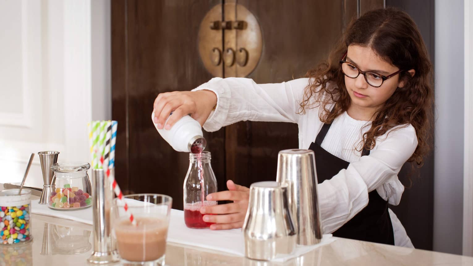 Girl with dark hair and glasses wearing apron, mixing mocktails