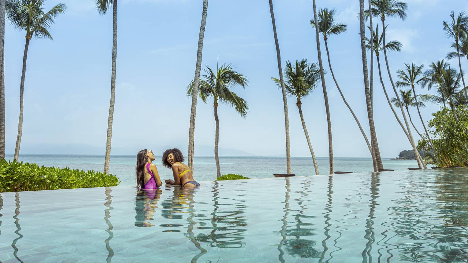 Two female guests laugh in the infinity-edge pool of CocoRum Bar