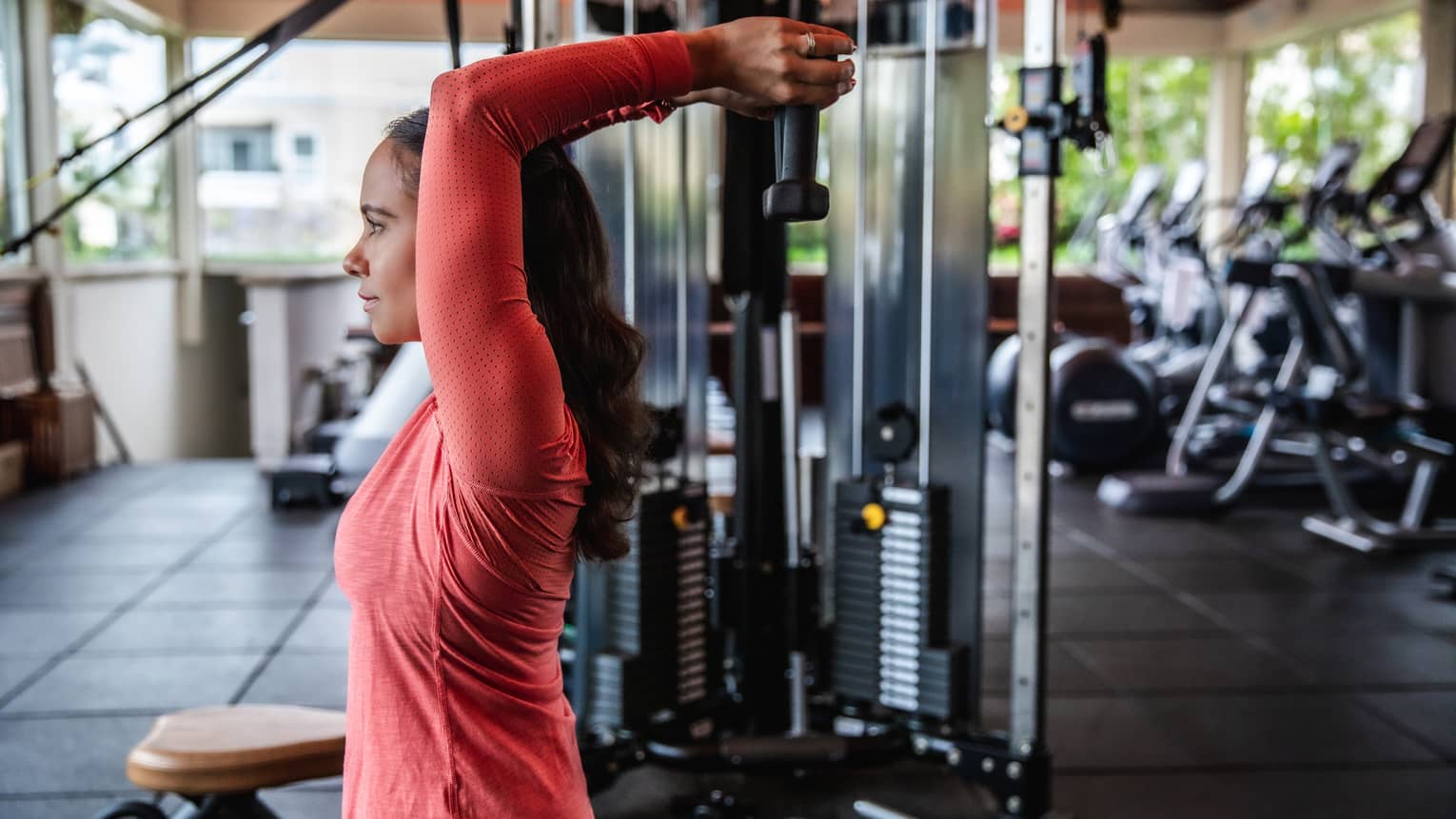 A woman lifts wights above her head at the gym