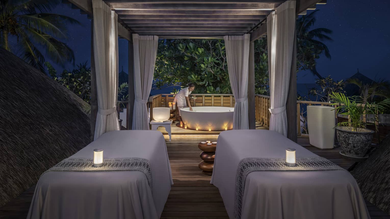Couples massage beds with glowing candles at outdoor spa pavillion at night