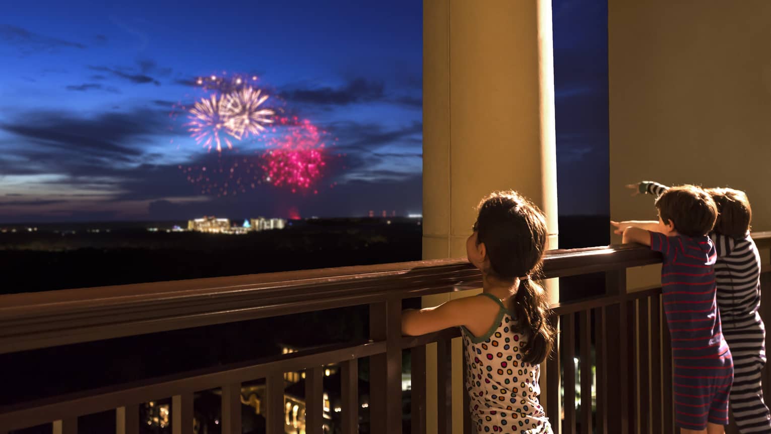 Young girl stands on Four Seasons Hotel balcony, watches colourful fireworks display over Walt Disney World resort