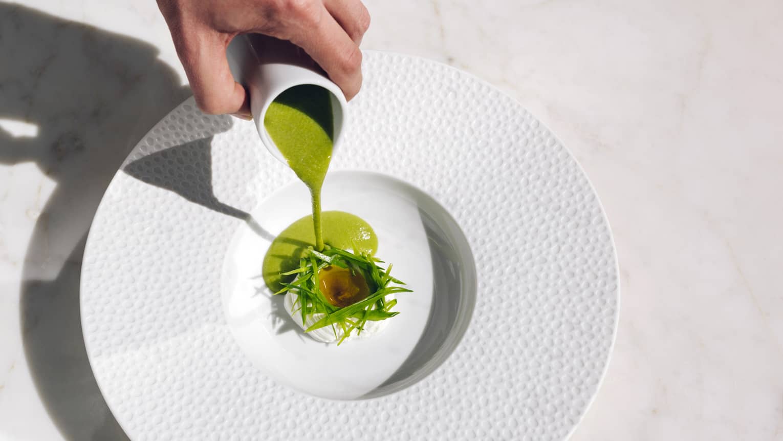 Spring Pea Soup being poured from cup into white bowl with green garnish