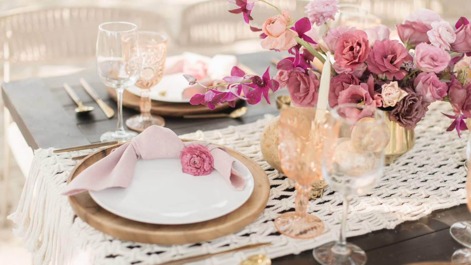 A table with wedding decorations of white plates, wine glasses, and light red and pink roses.
