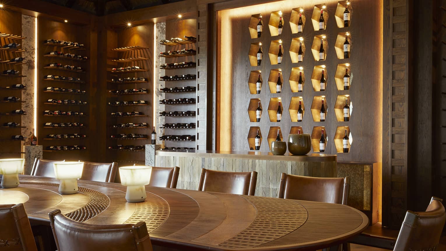 Contemporary wine cellar with uplit bottles on walls and oval-shaped dining table in centre