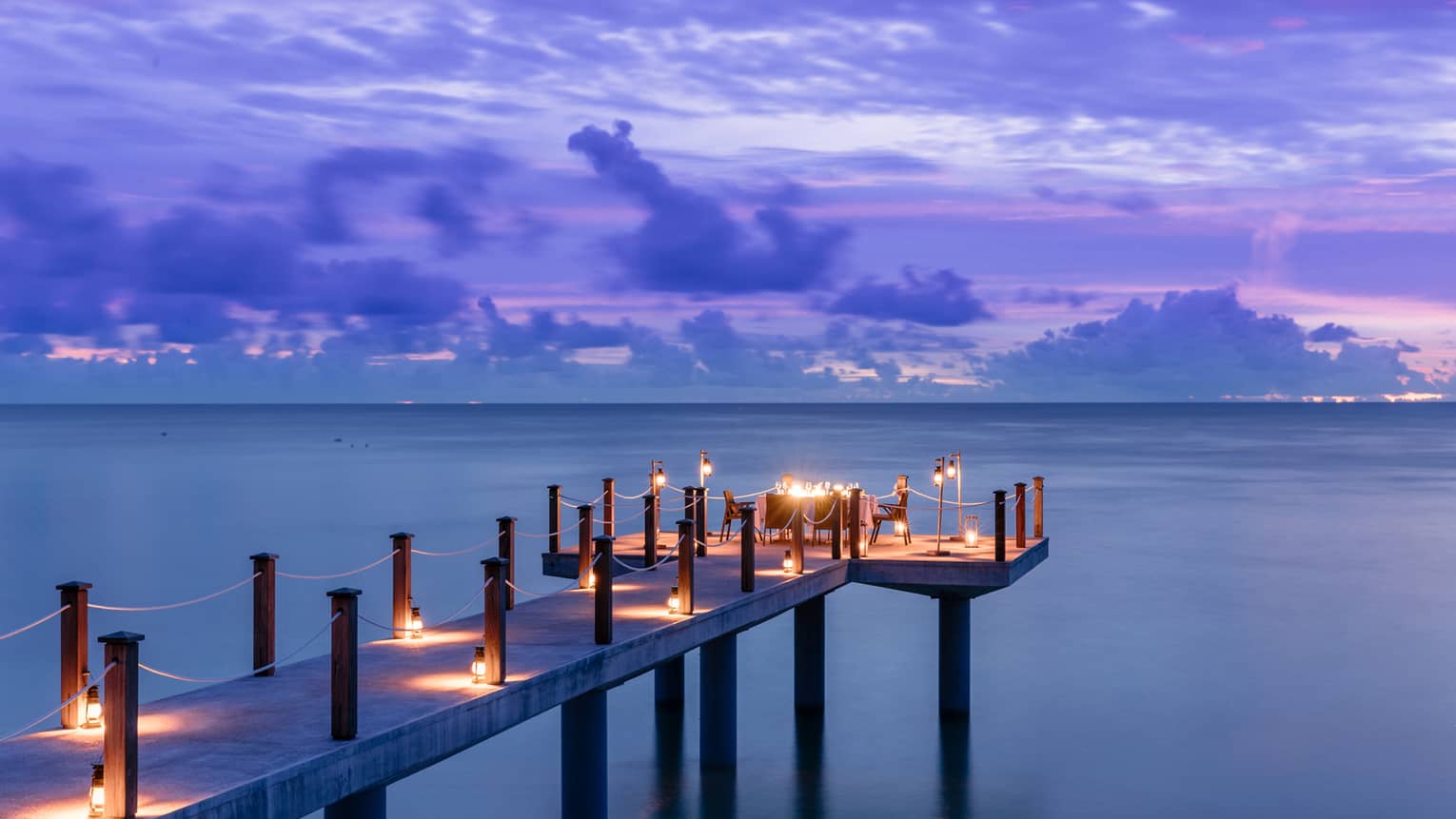 Candlelit jetty off Desroches Island with purple sunset hues