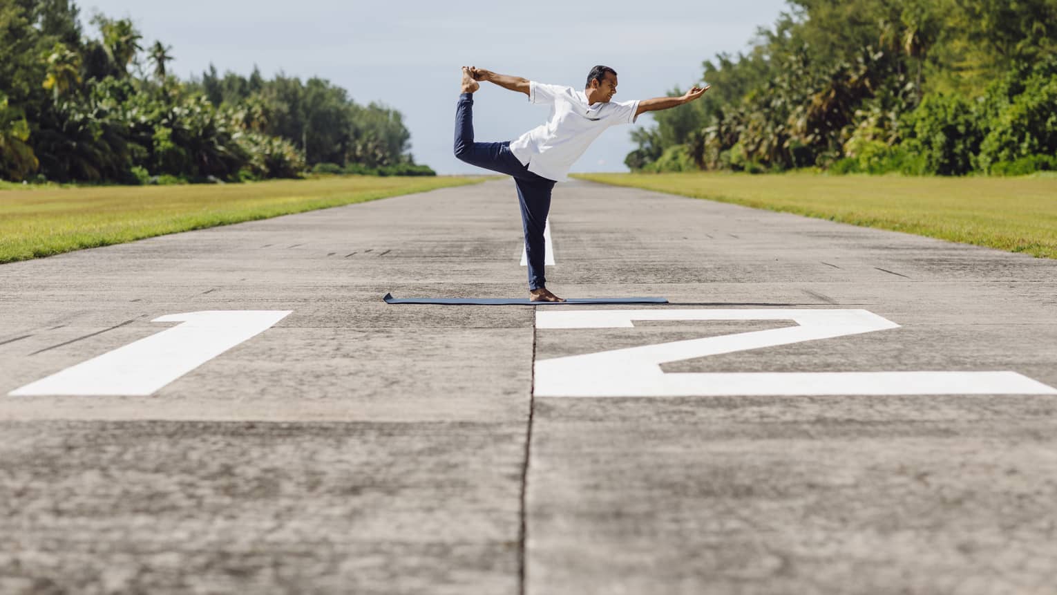 A man doing yoga – specifically ballerina pose – on an airplane runway