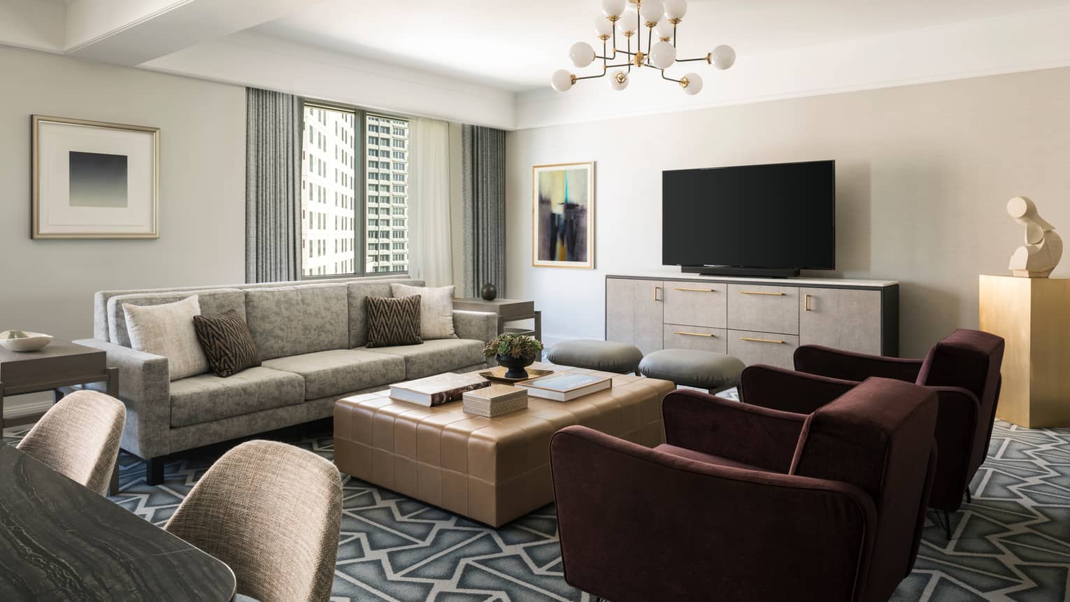 Living room with beige sofa, large square coffee table, two burgundy arm chairs, graphic carpeting