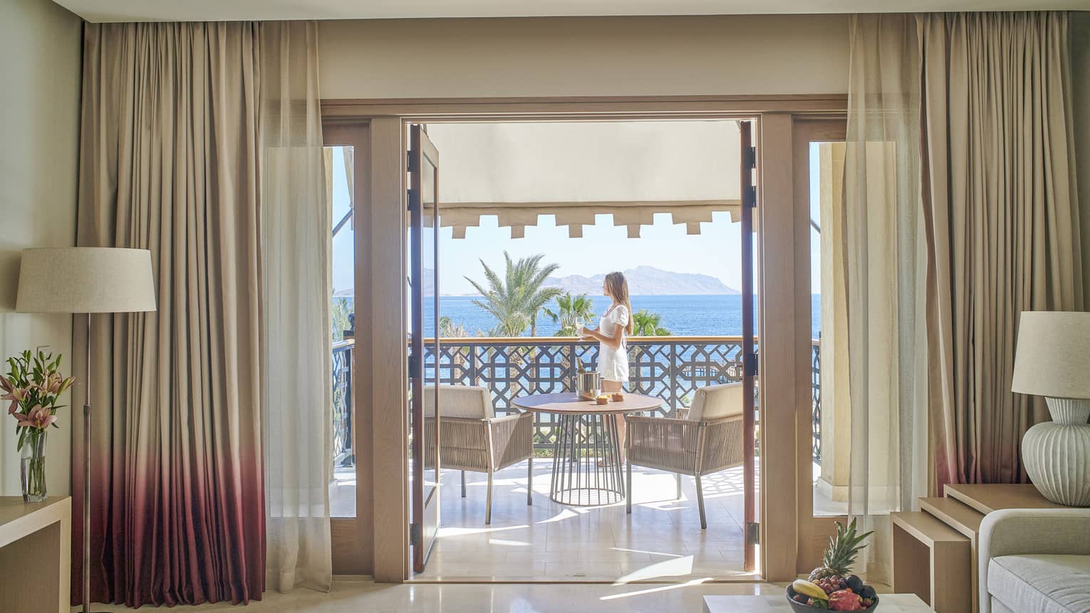 Woman stands on sea-view balcony connected to a hotel suite