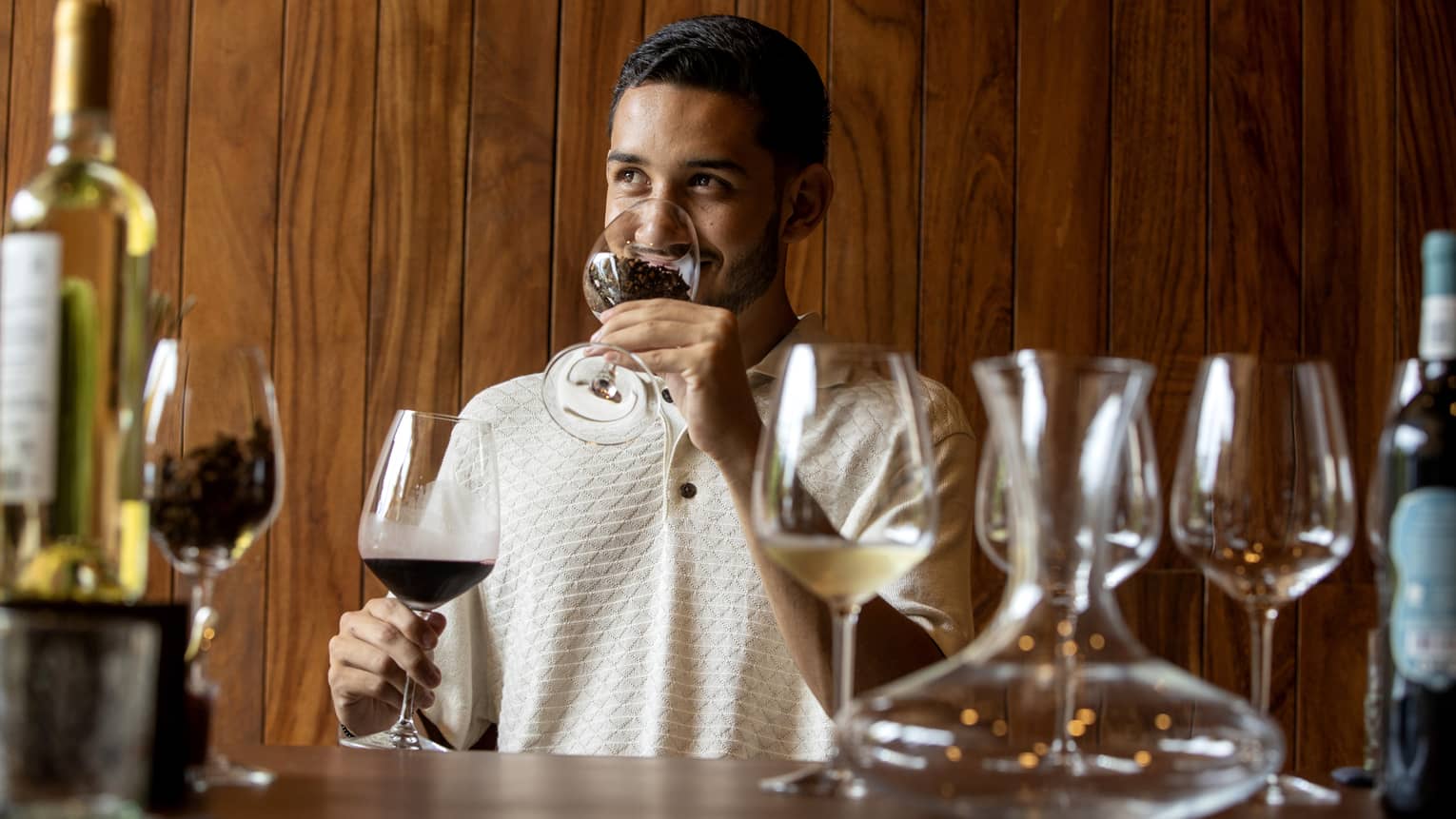 At a wine tasting, a guest smells coffee beans in a glass before tasting the glass of dark red wine held in his other hand. 