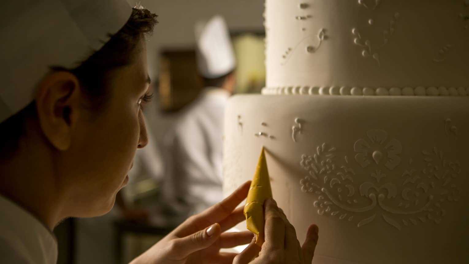 Pastry chef adds decorative details to tiered white wedding cake