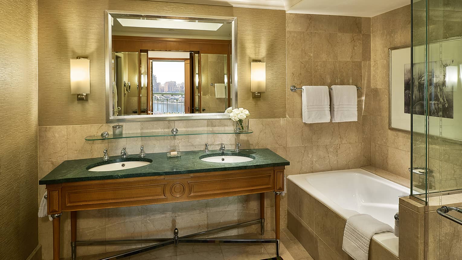Guest room bathroom with double green granite?topped vanity, deep soaking tub,  mirror flanked by lighted wall sconces, glass shower