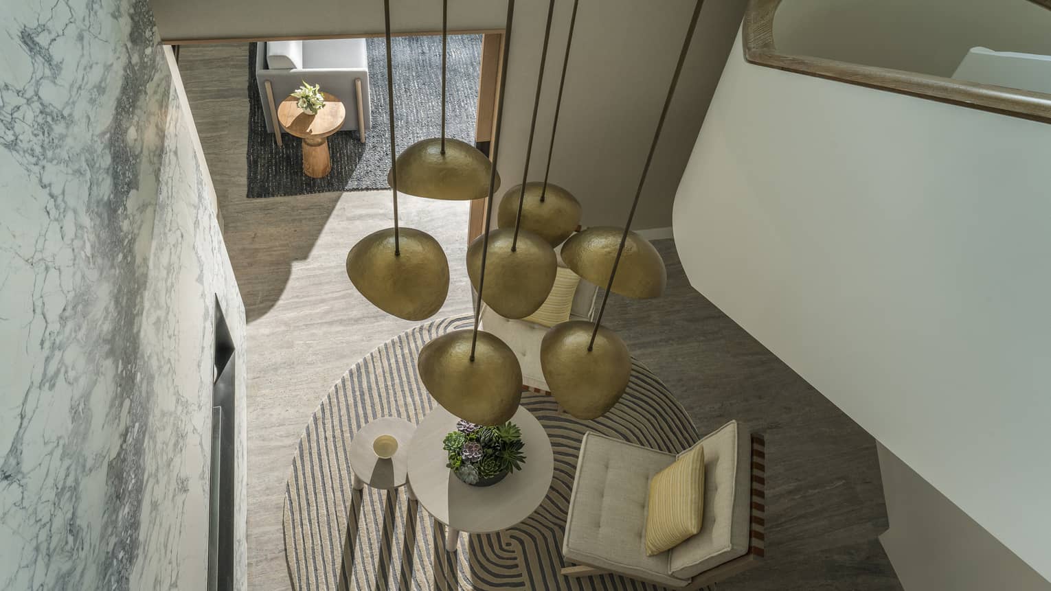 Aerial view of Arion Riviera Suite from staircase, round area rug, white accent chair and coffee table, modern gold lighting