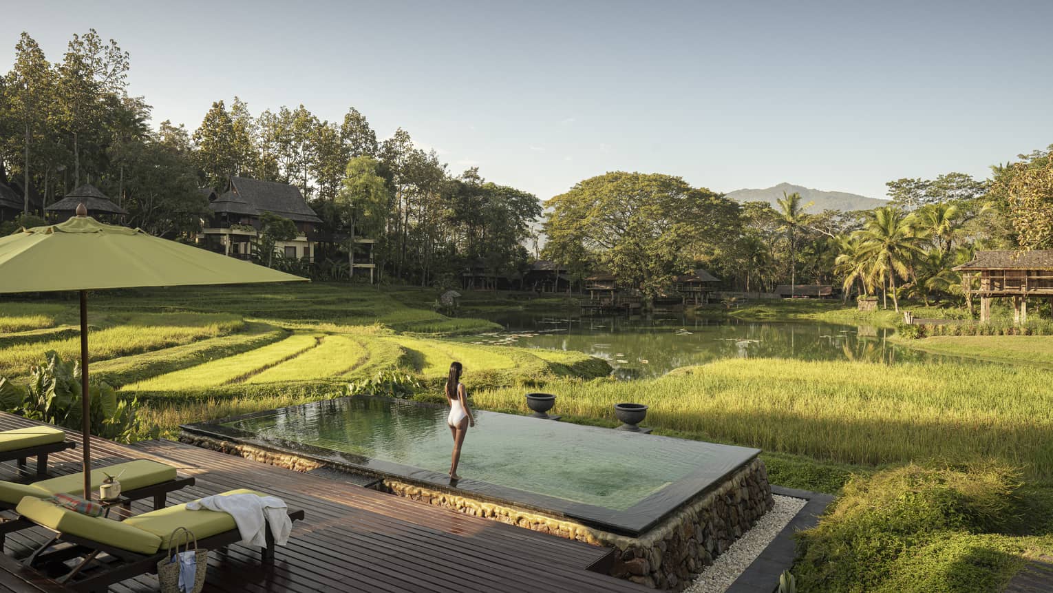 Woman in white bathing suit stands in front of pool overlooking rice paddies