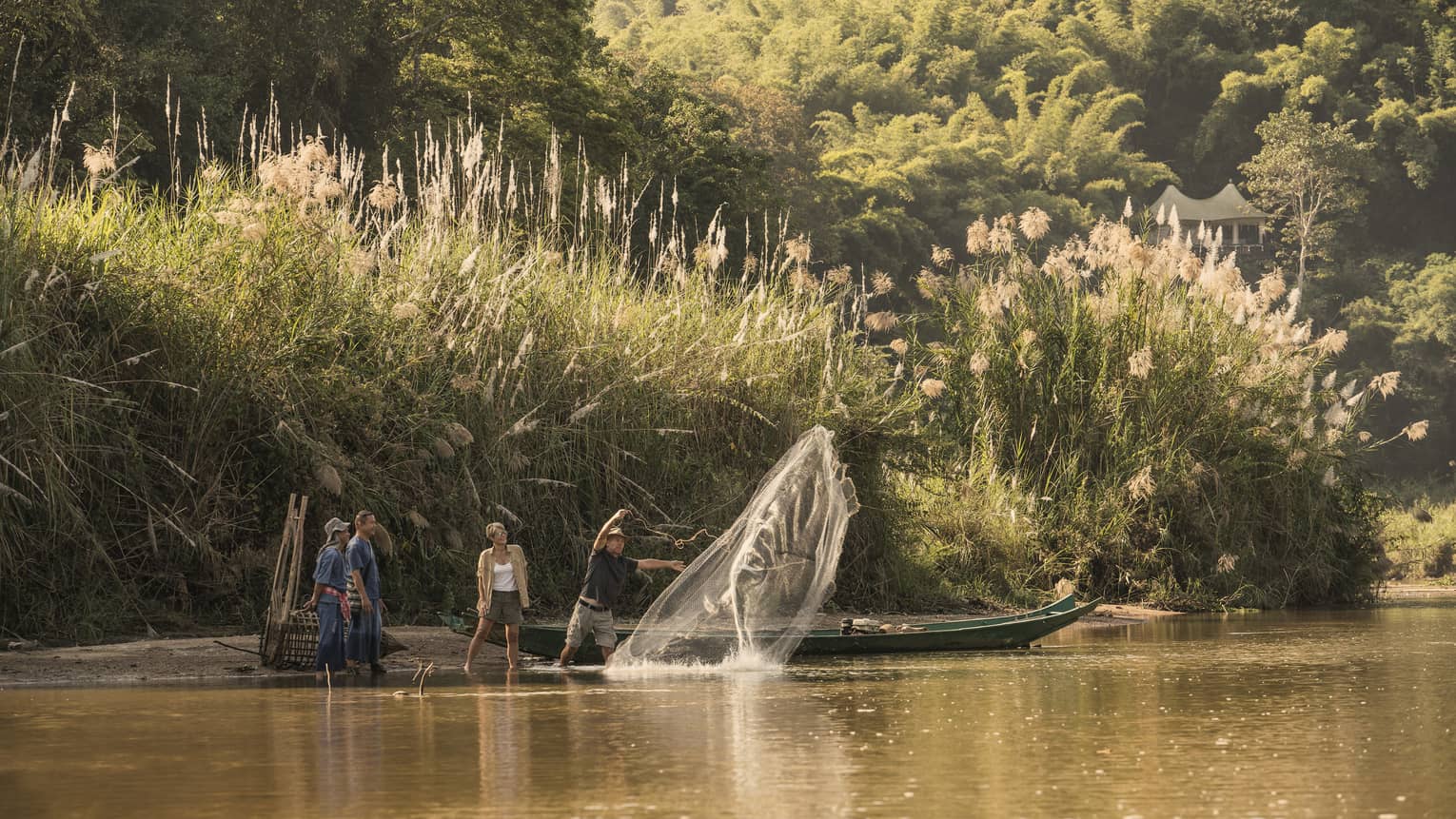 Man throws traditional Thai fishing net from boat into river during group activity