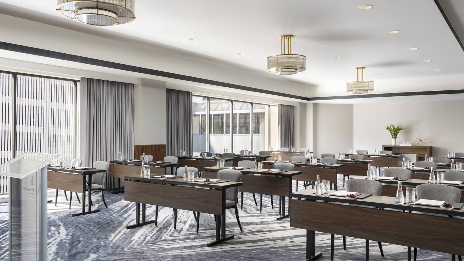 A well lit meeting room with dark wood tables and chairs facing a podium.