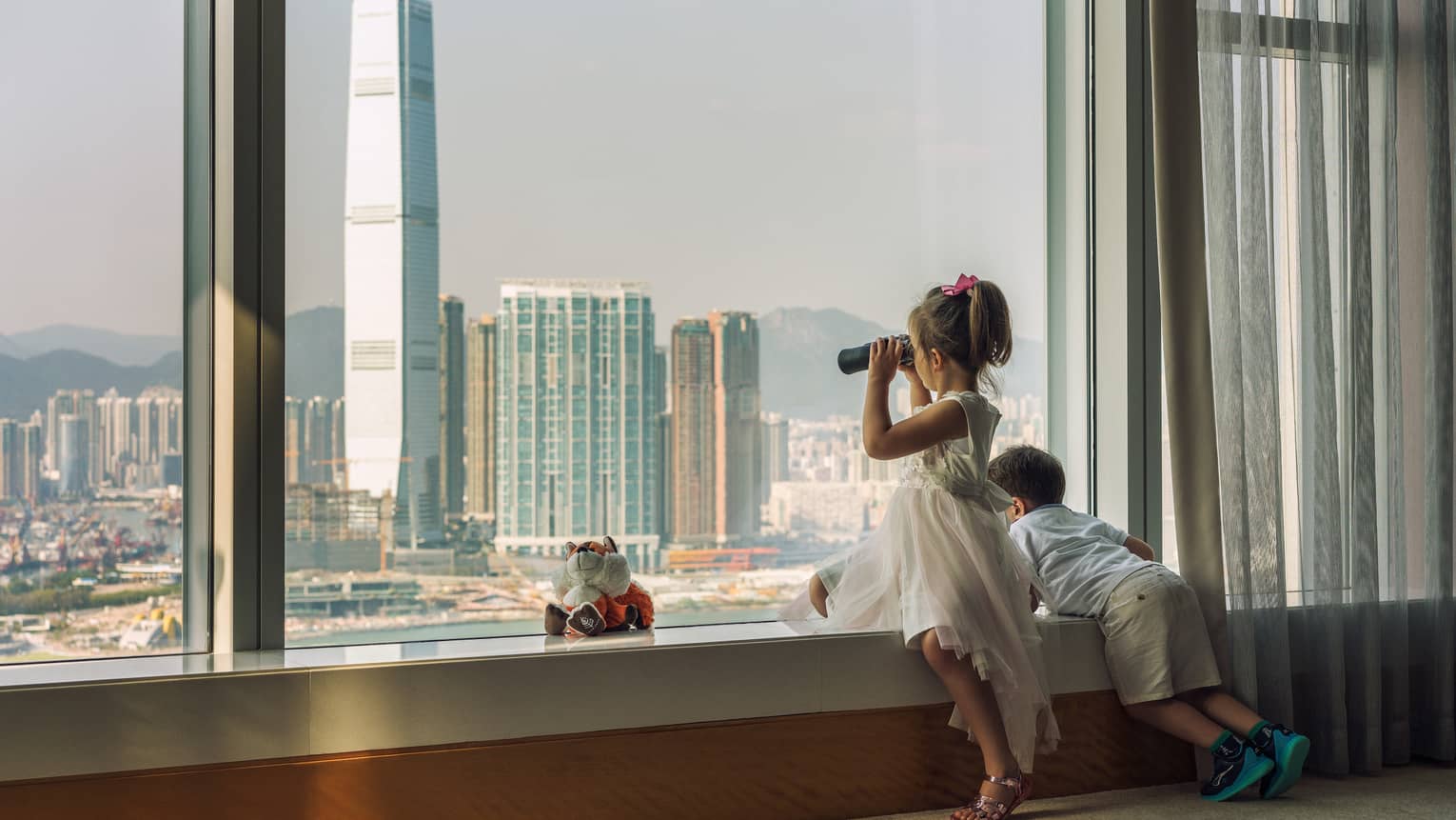 Young boy and girl looking out hotel window to Hong Kong cityscape