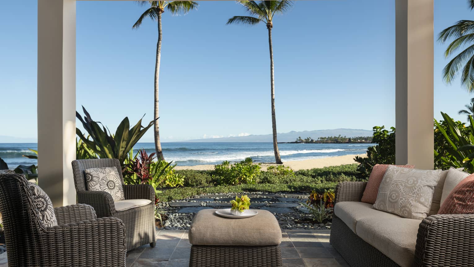 Covered lanai with dark wicker sofa and two matching arm chairs, ottoman, beach view