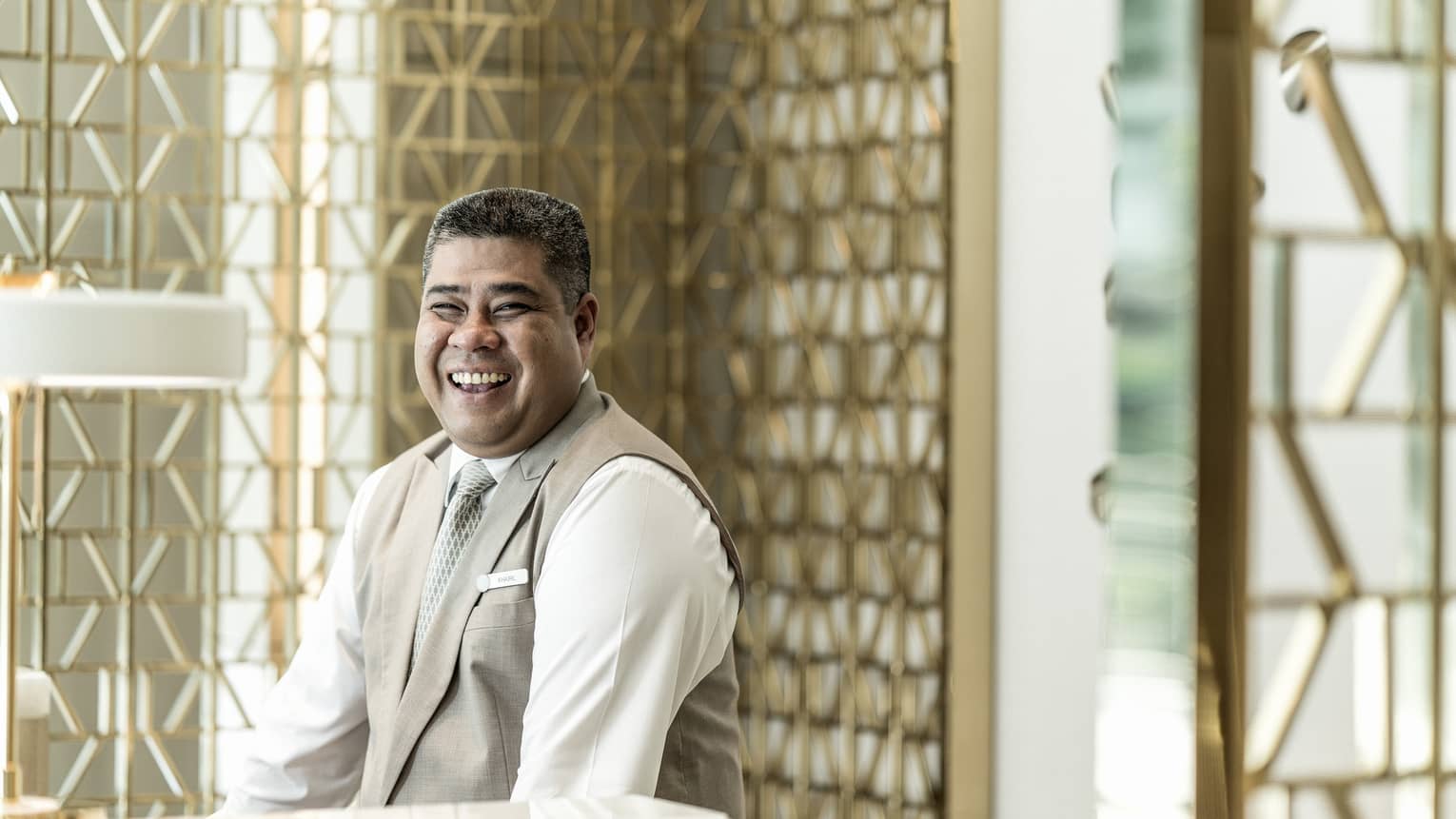 Smiling private concierge wearing Four Seasons uniform in front of gold accent wall