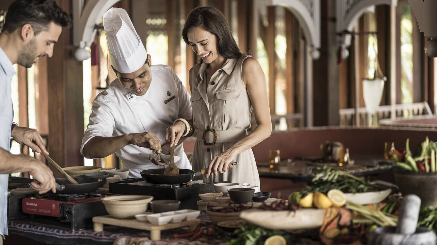 A chef is instructing a man and woman in the Ikan Ikan Cooking Class