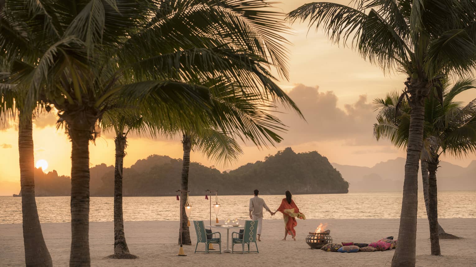 A man and woman on a beach having a Punta chintai private dinner at Four Seasons Langkawi