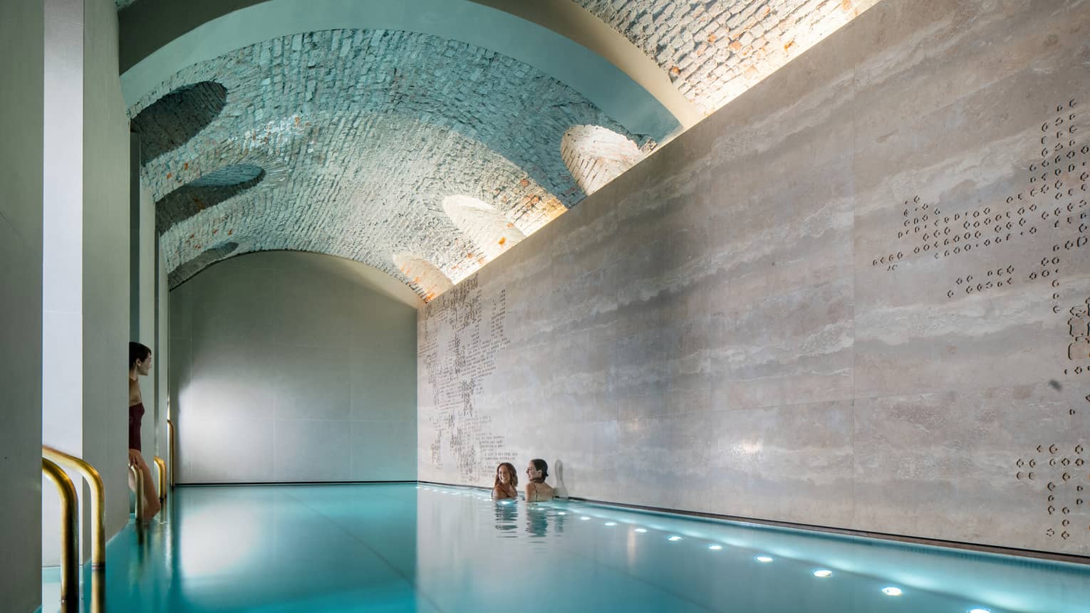 Three women soaking in a modern indoor pool with an arch ceiling