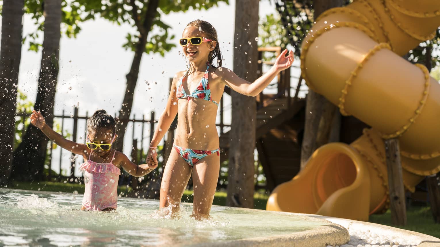 Two young girls splash in the kiddie pool, a water slide in the background