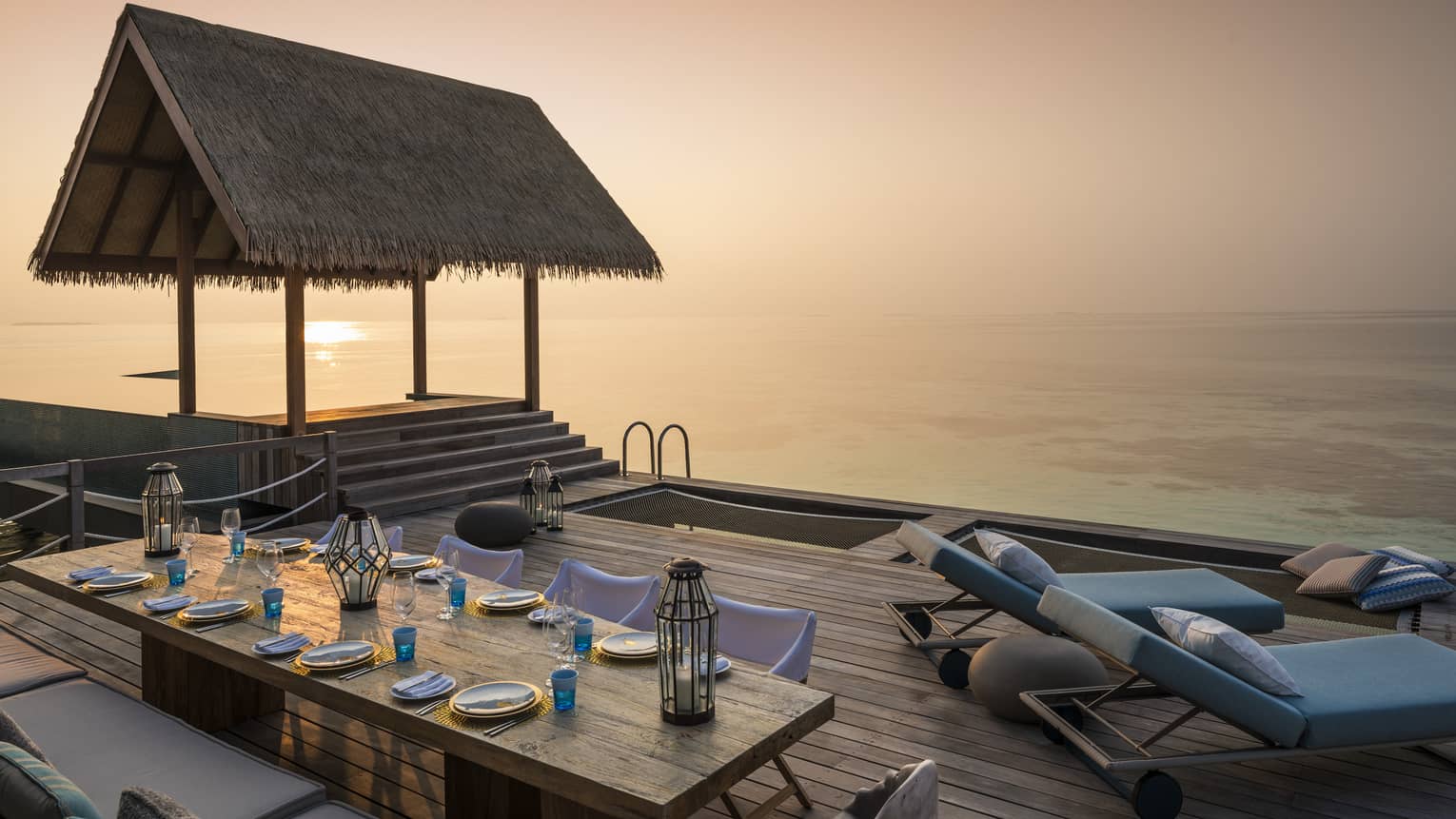 Two-Bedroom Water Villa thatched roof pavilion over long private dining table on deck at sunset