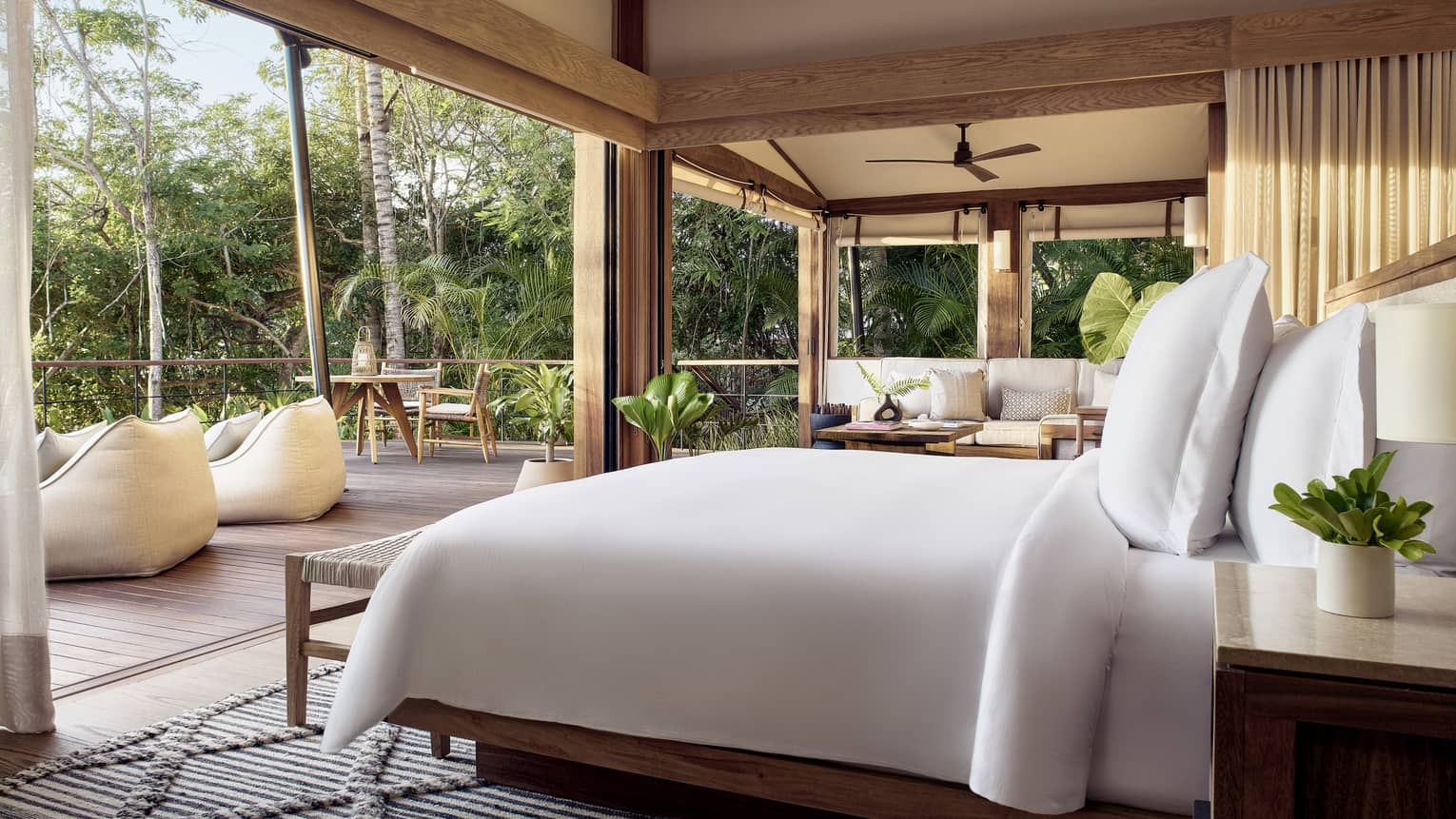 Bedroom of a luxury tent, open to a deck and surrounded by tropical forest