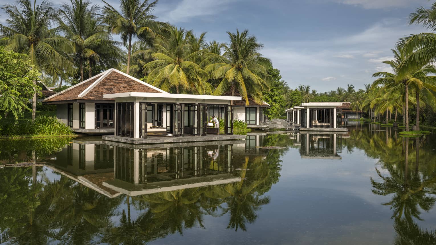Overwater Heart of Earth spa villa staff folds white towels on deck, reflection in water