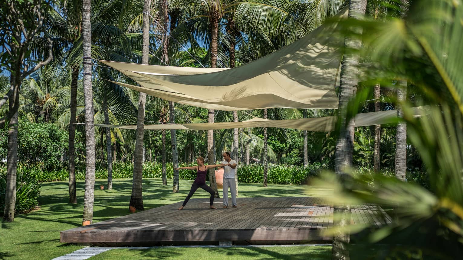 Yogi helps two people with yoga poses on wood platform under canopies