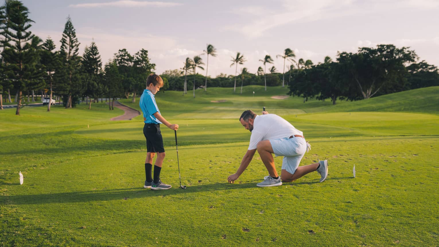 Man and young son play golf on the green, blue sky and palm trees in background 
