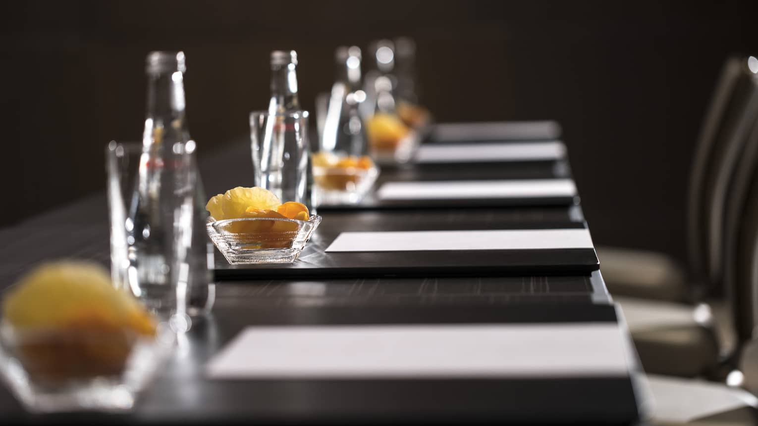 Row of glass bottles, small dishes with dried fruits, meeting agendas along boardroom table