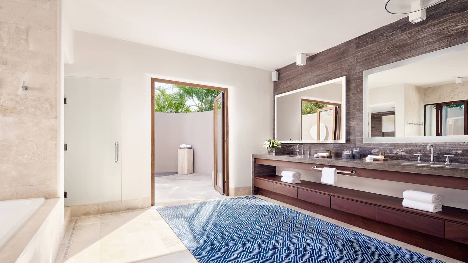 Arena Beach House bathroom with double vanity and mirrors, blue patterned area rug, door to patio