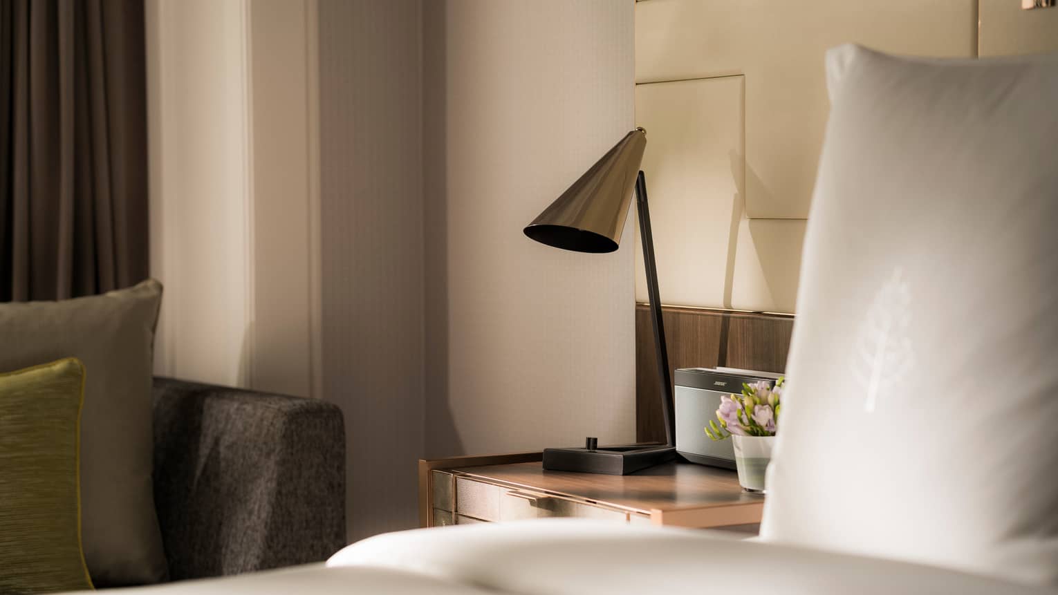 Modern silver lamp on nightstand beside alarm clock, bed 