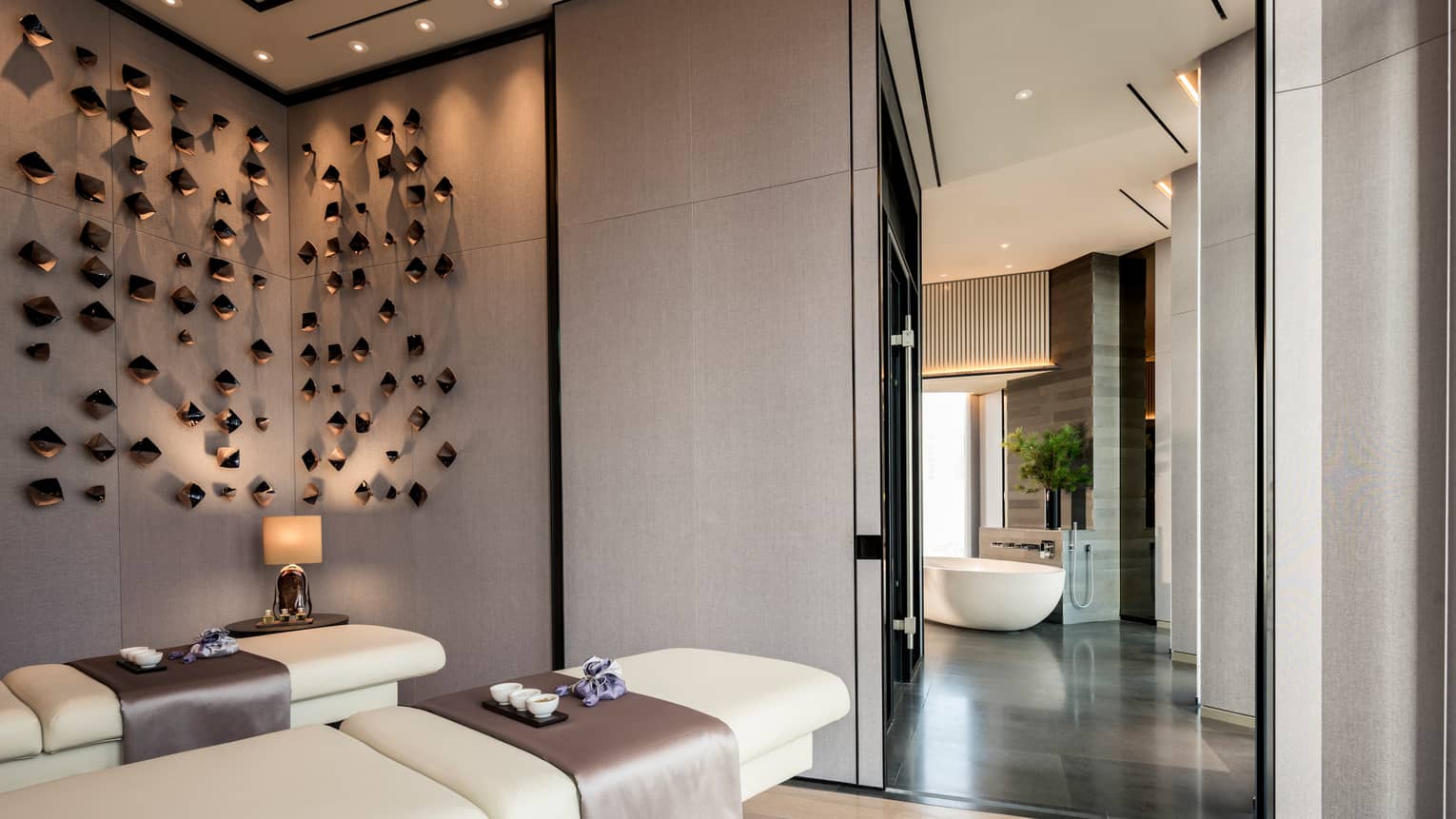 Couples massage beds under modern wall sculptures by hall leading to spa tub