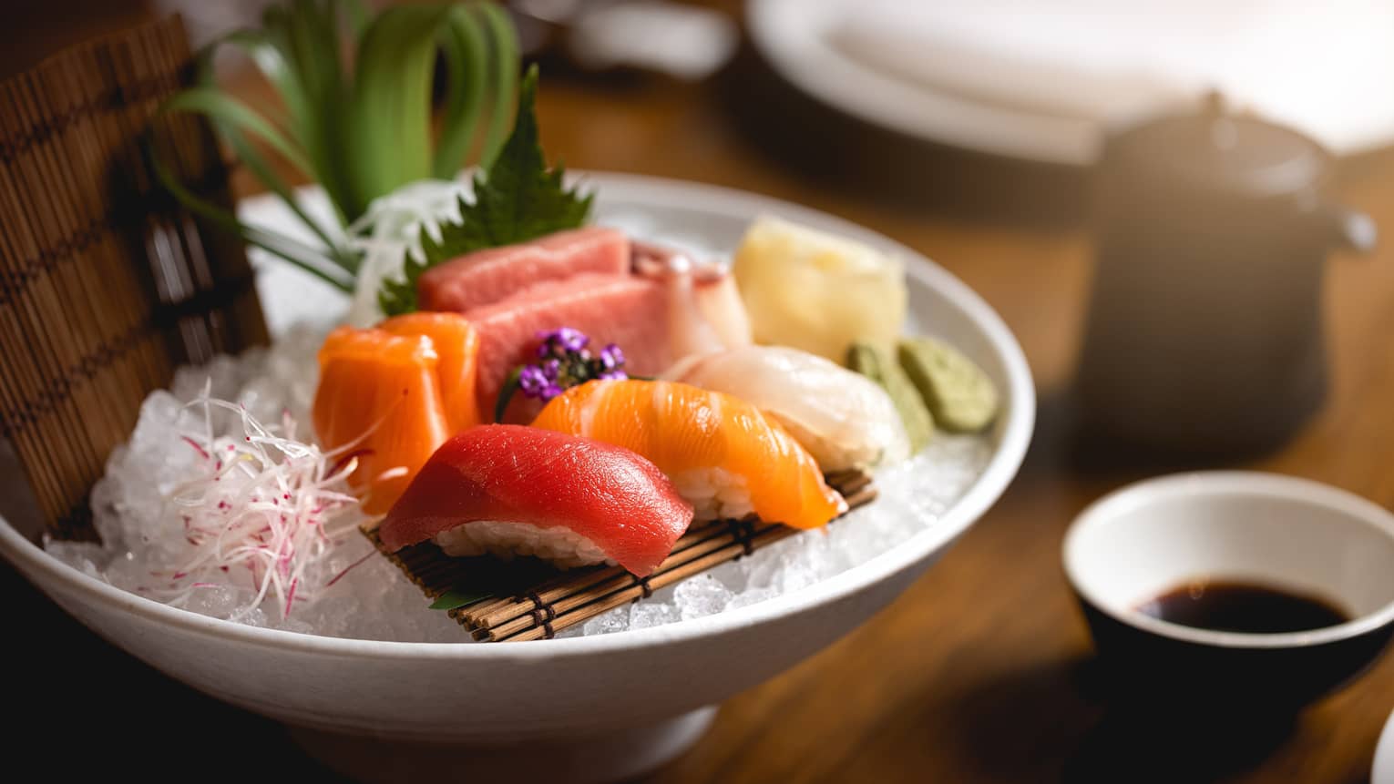 Colourful sashimi and nigiri on bamboo mat atop crushed ice in white bowl