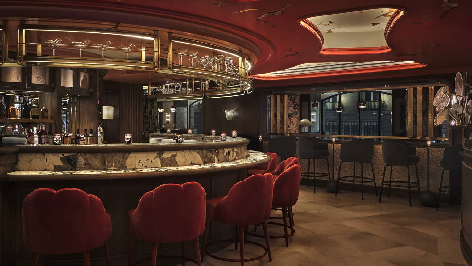 Moody bar and lounge with red upholstered chairs, curved bar, red-lit ceiling features
