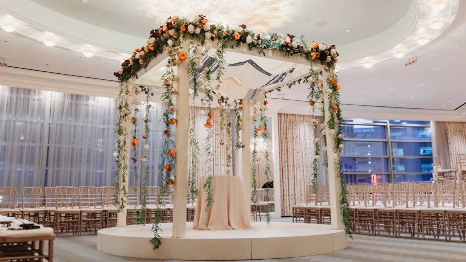 An alter made of white wood with bright flowers covering it, in a room with rows of seats.