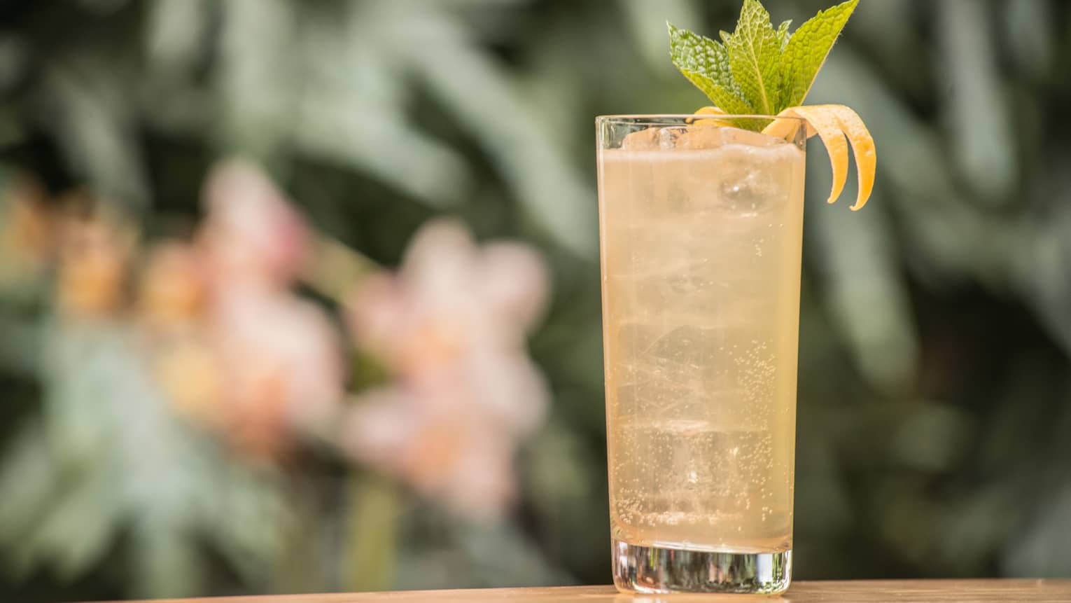 A tall glass filled with a yellow cocktail and several mint leaves. 