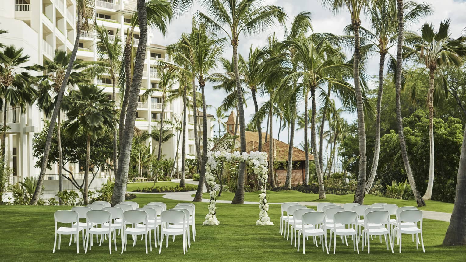 Outdoor wedding reception on event lawn, rows of white chairs face altar beneath palm trees