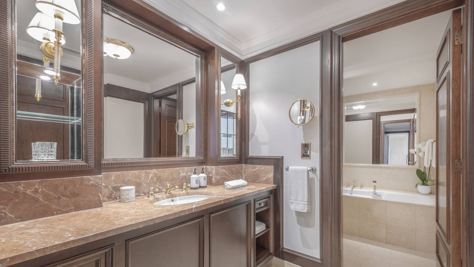 A large bathroom with a large countertop, sink, large mirror and a separate room with a bath.