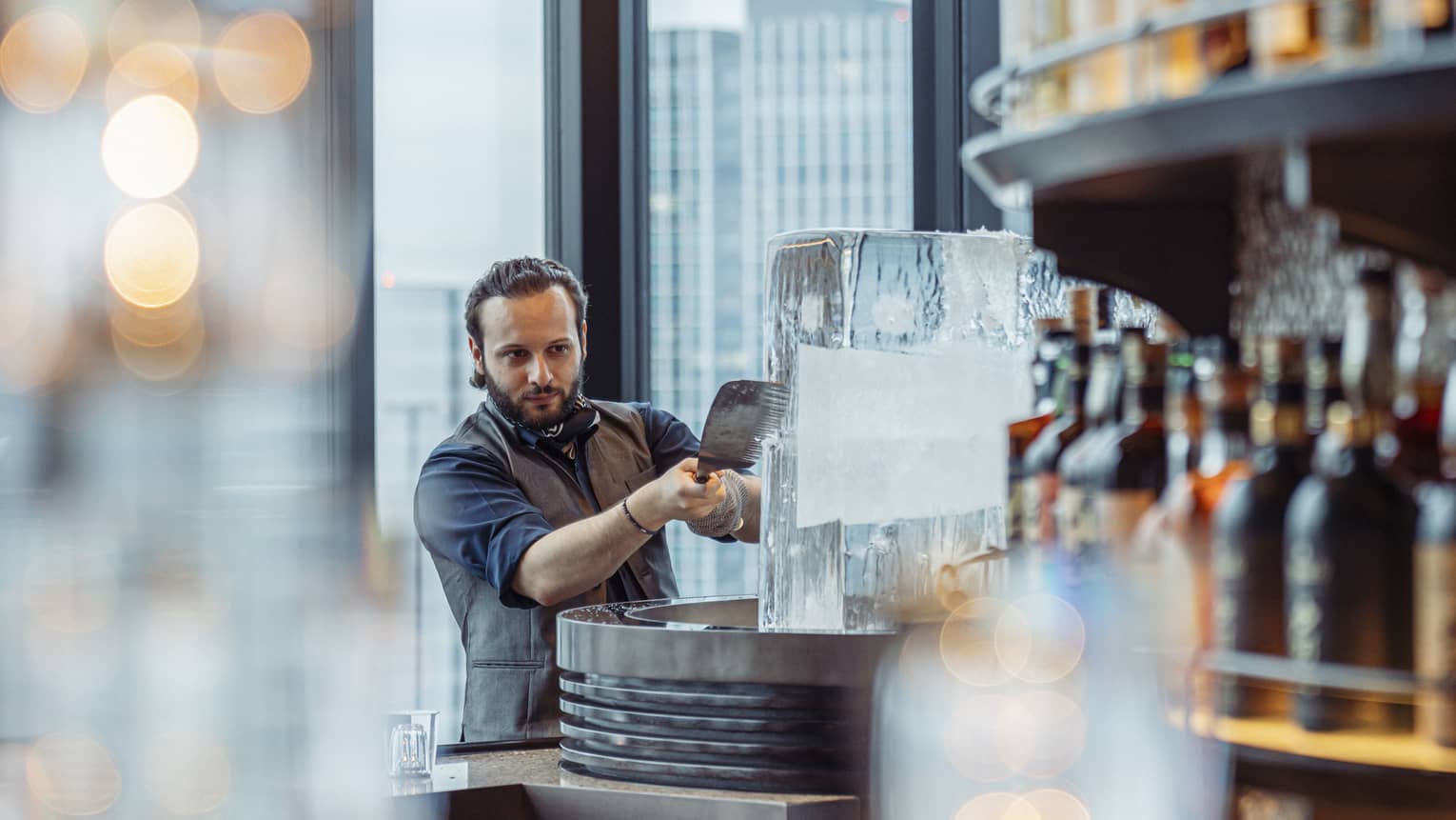 Male bartender shaves ice off a large ice block at luxury hotel bar