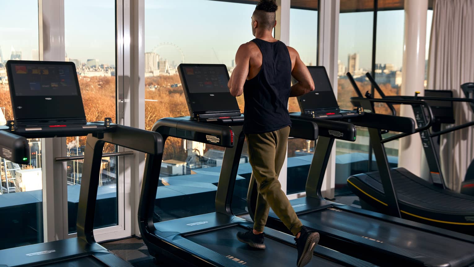 A man running on a treadmill near large windows.