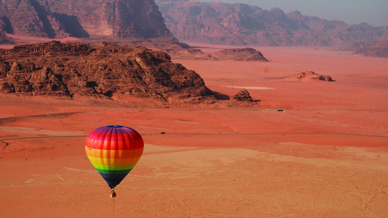 Rainbow hot air balloon flying over red sand in Jordan desert