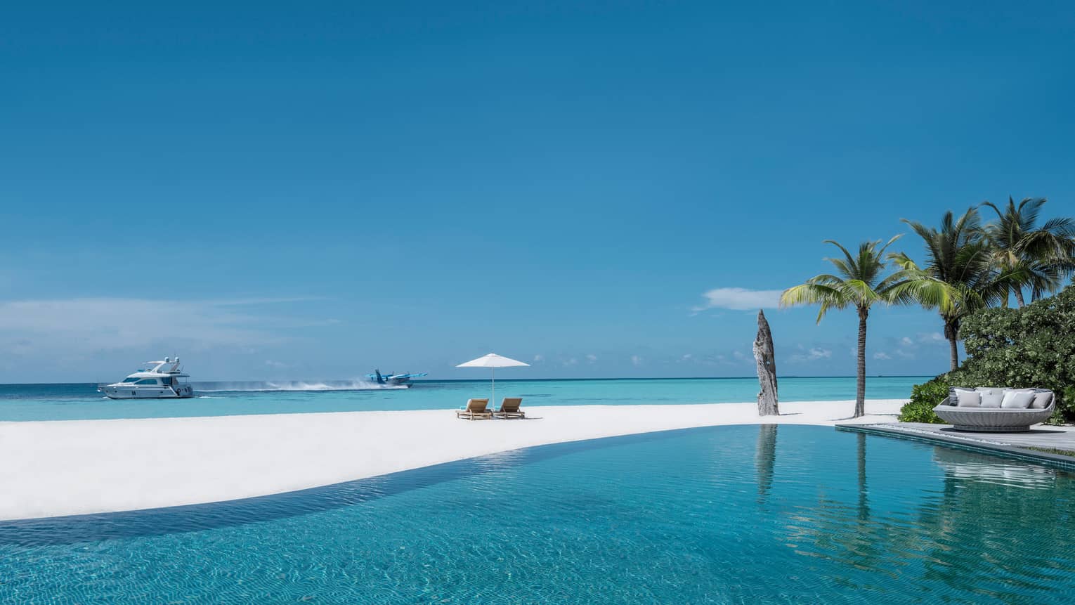 Infinity swimming pool by white sand beach, plane and catamaran boat in lagoon