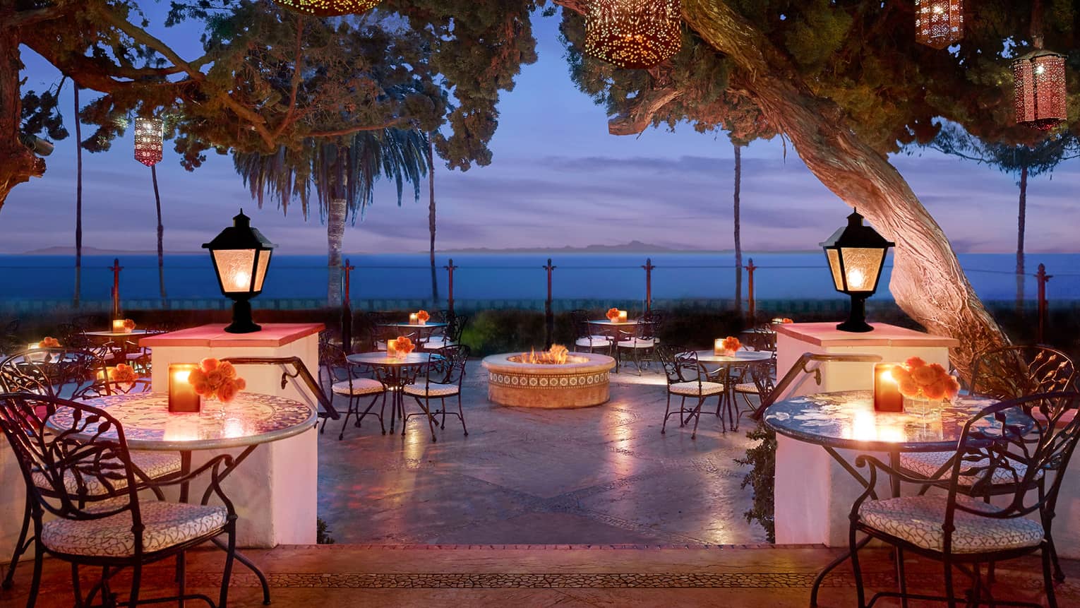Bella Vista patio at dusk with candle-lit tables under lanterns on posts, hanging from trees