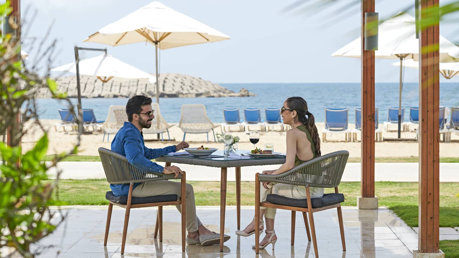 Smiling couple dines at patio table on private pergola near white sand beach