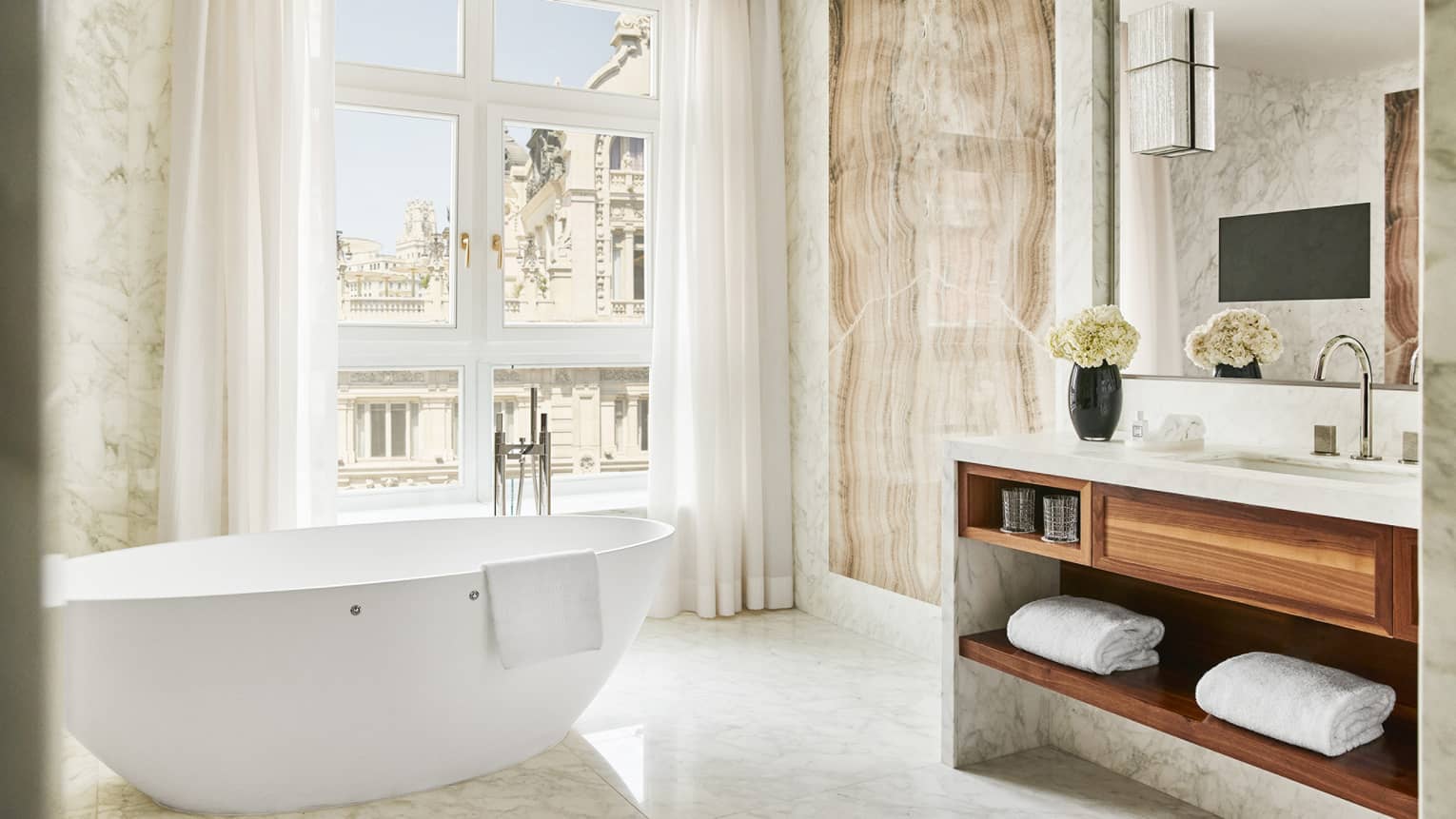 Bathroom with wall of windows, free-standing white tub, vanity with wooden shelves